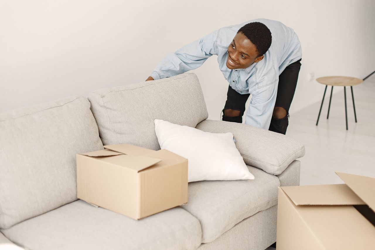 A young man is smiling as he organizes cardboard boxes in a contemporary living room.